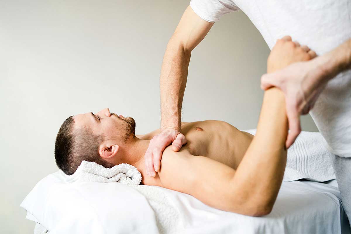 Massage therapist stretching a client's arm and working on the shoulder and chest as he lies on a treatment table