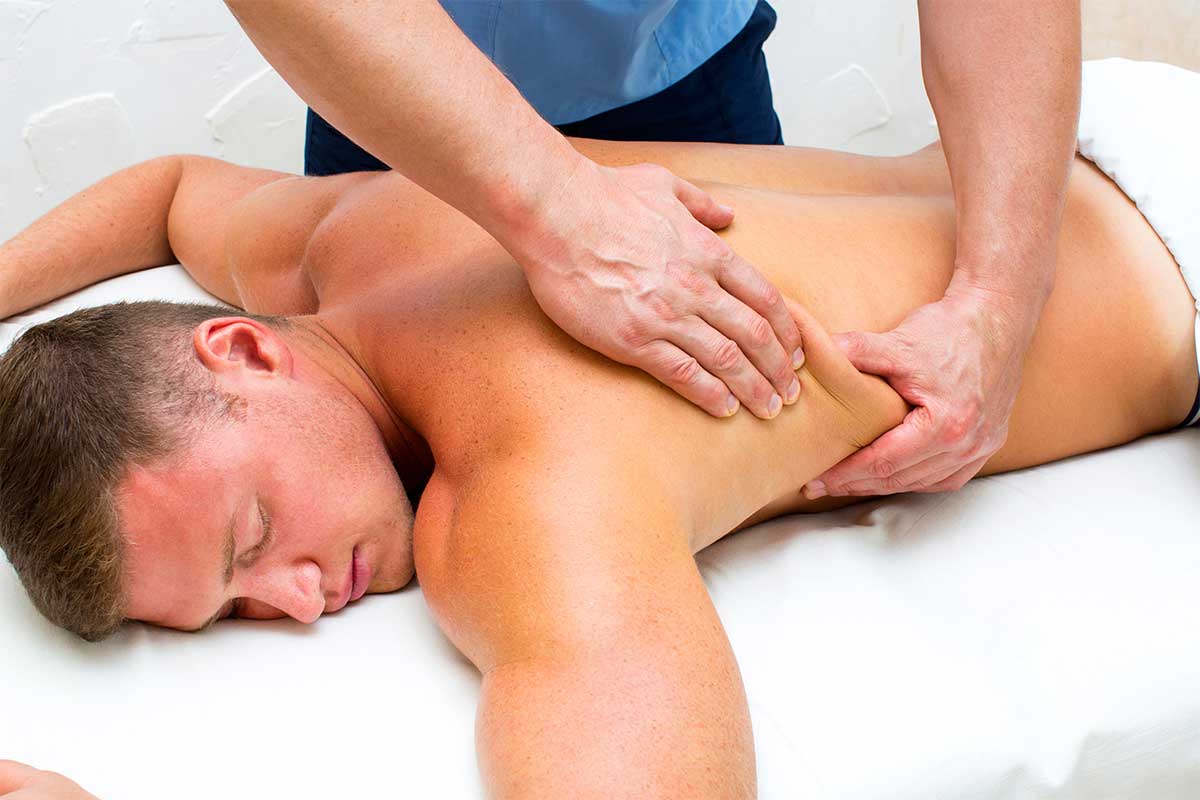 Therapist massaging a client's shoulder blade area as he lies face down on a massage table