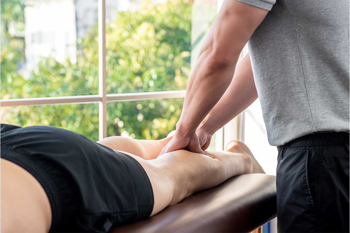 Sports massage therapist working on a client's calf muscles beside a large window