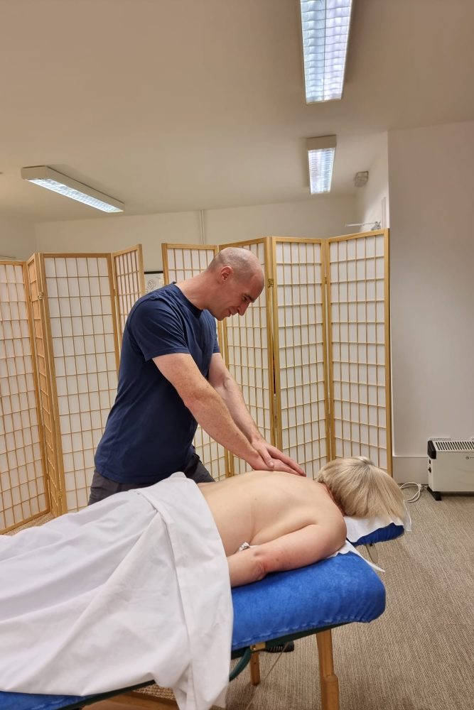 Massage therapist giving a client a back massage on a treatment couch in a clinic room